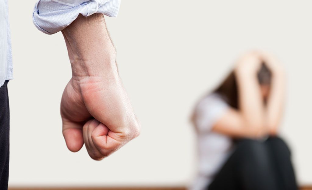 En knytnäve och en person i förgrunden som hukar sig och håller för huvudet