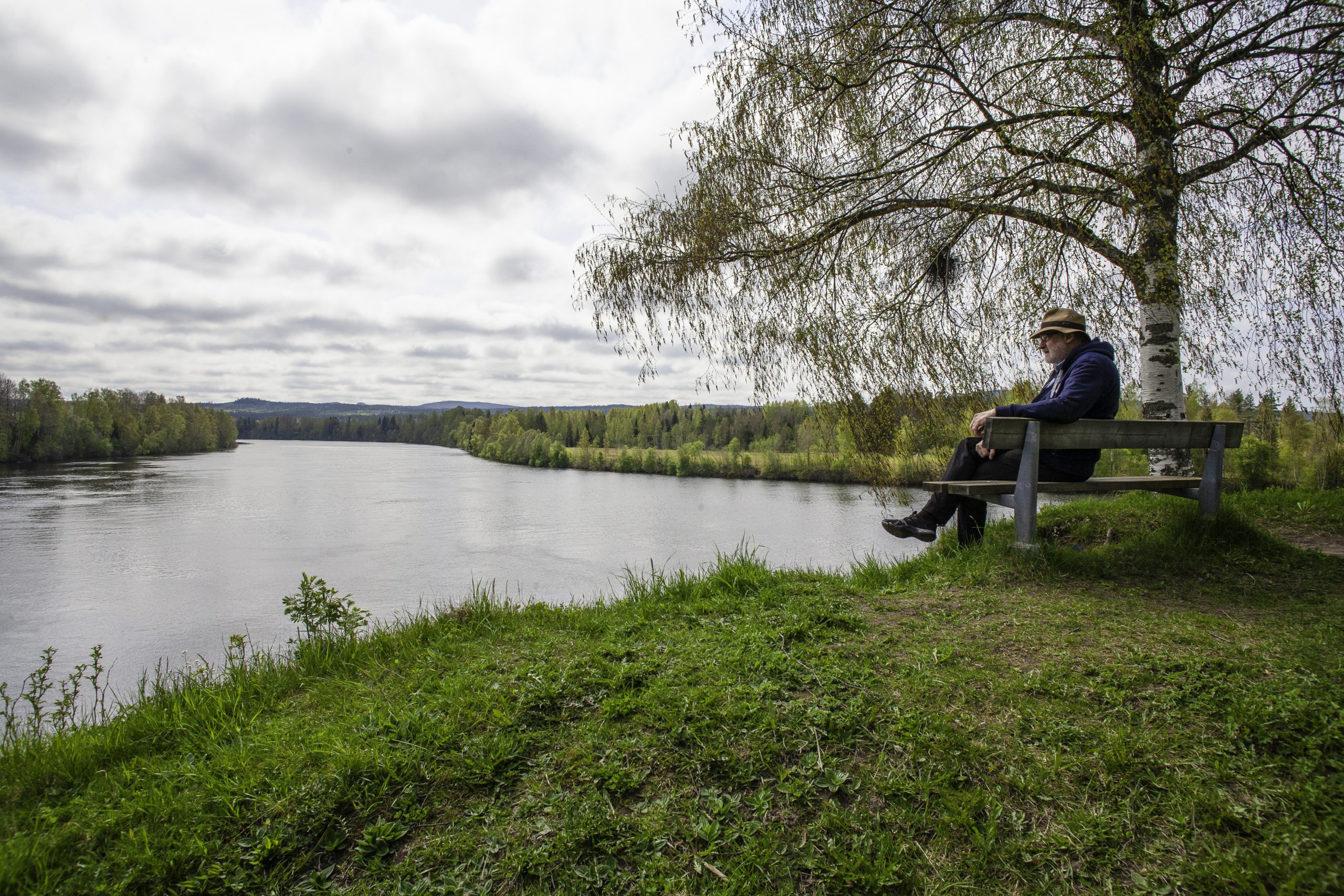 En person sitter på en bänk vid vatten.