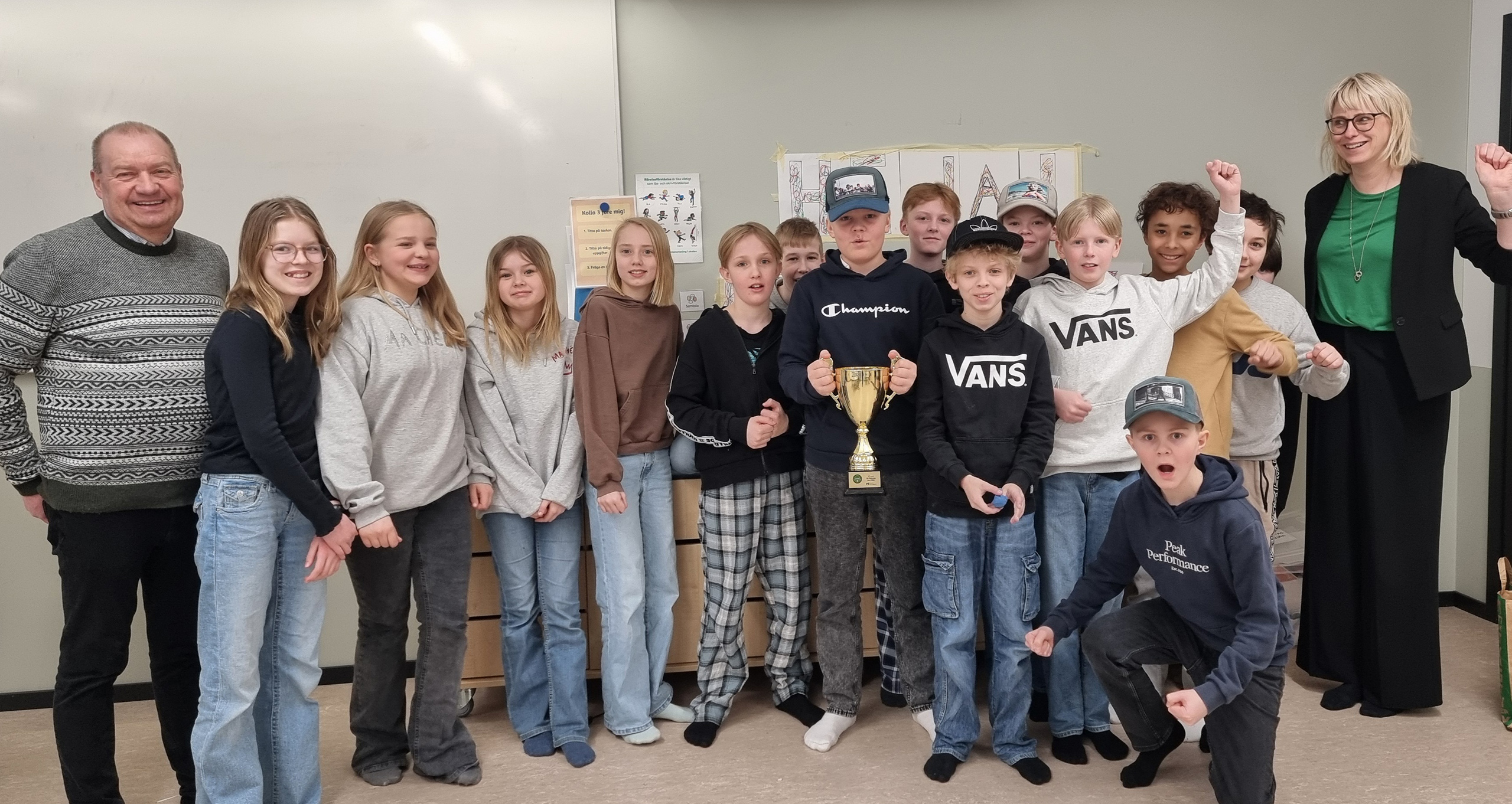 14 barn och två vuxna står i klassrum.